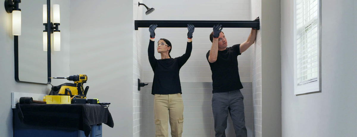 Two people installing a shower door track in a bathroom.