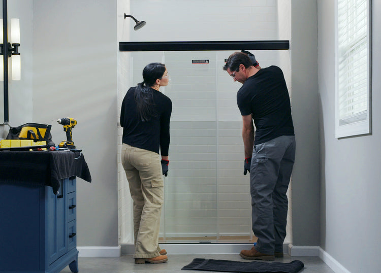 Two people installing a glass shower door in a bathroom.